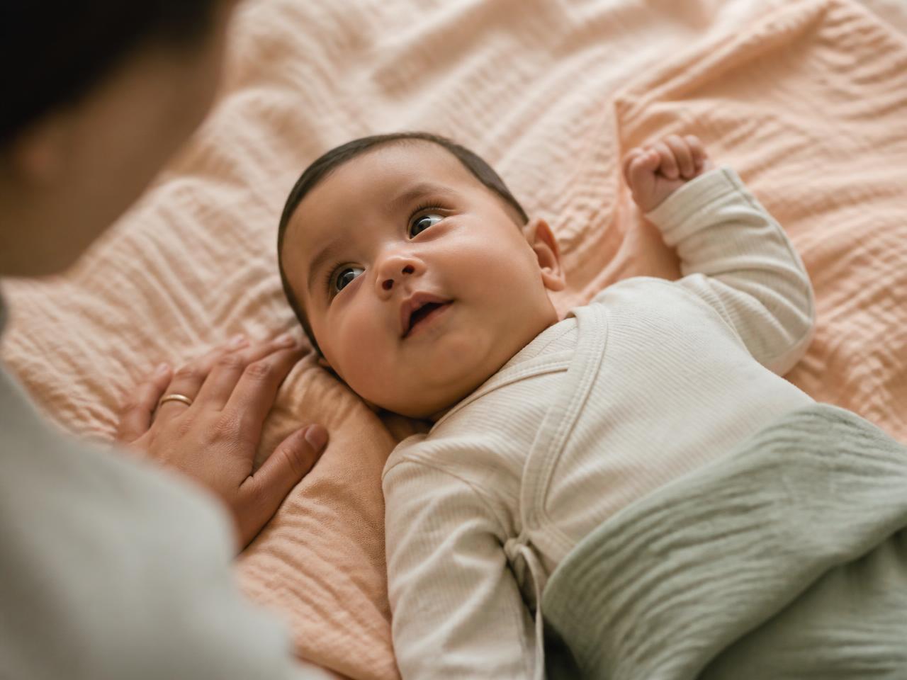 Bebé recostado sobre una manta suave mirando a su madre